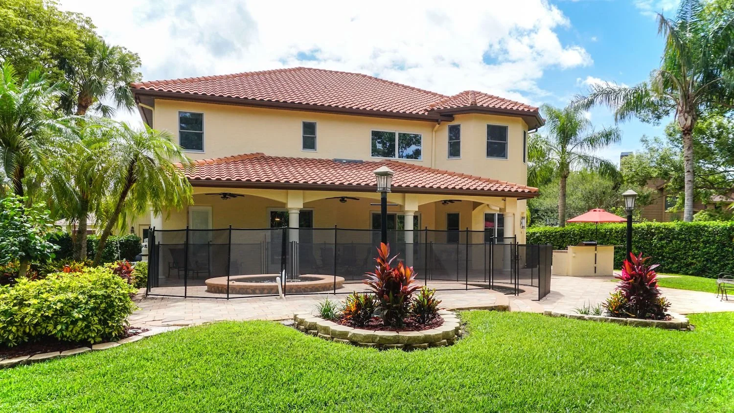 Two-story home with clean stucco walls and a barrel tile roof beside a screened patio